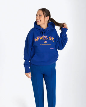 Entdecken Sie den stylischen 'APRES SKI HOODIE' von Strawanza, ideal für Outdoor-Abenteuer. Das Model präsentiert diesen trendigen blauen Hoodie in einer natürlichen Kulisse, die Funktionalität und Modebewusstsein vereint. Der Hoodie zeichnet sich durch sein starkes blau und den Siebdruck im Retro Stil aus. Perfekt für Berg- und Skiabenteuer. Hieran einem Frauenmodel zu sehen. 