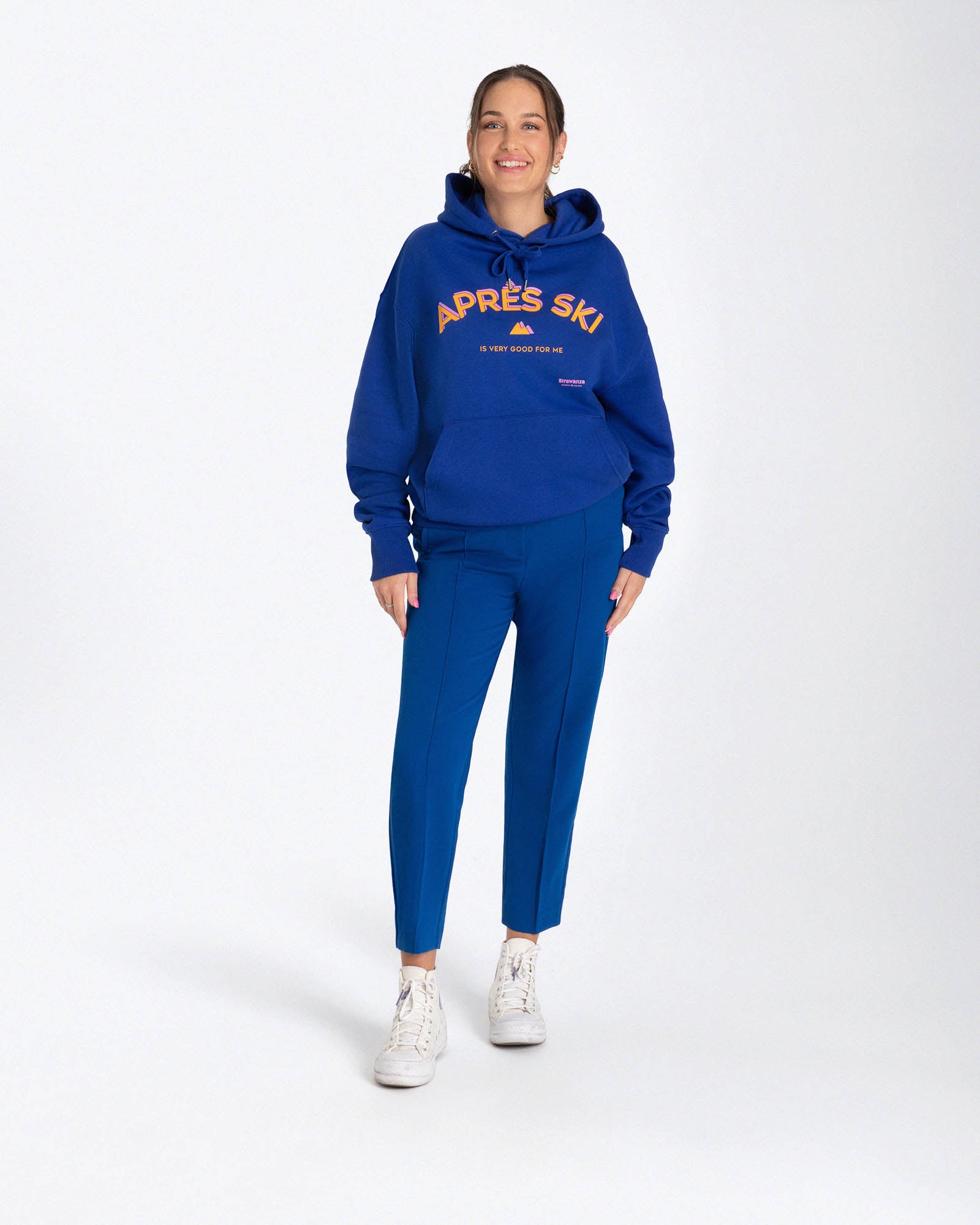 Entdecken Sie den stylischen 'APRES SKI HOODIE' von Strawanza, ideal für Outdoor-Abenteuer. Das Model präsentiert diesen trendigen blauen Hoodie in einer natürlichen Kulisse, die Funktionalität und Modebewusstsein vereint. Der Hoodie zeichnet sich durch sein starkes blau und den Siebdruck im Retro Stil aus. Perfekt für Berg- und Skiabenteuer. Hier an einem Frauenmodel zu sehen. 